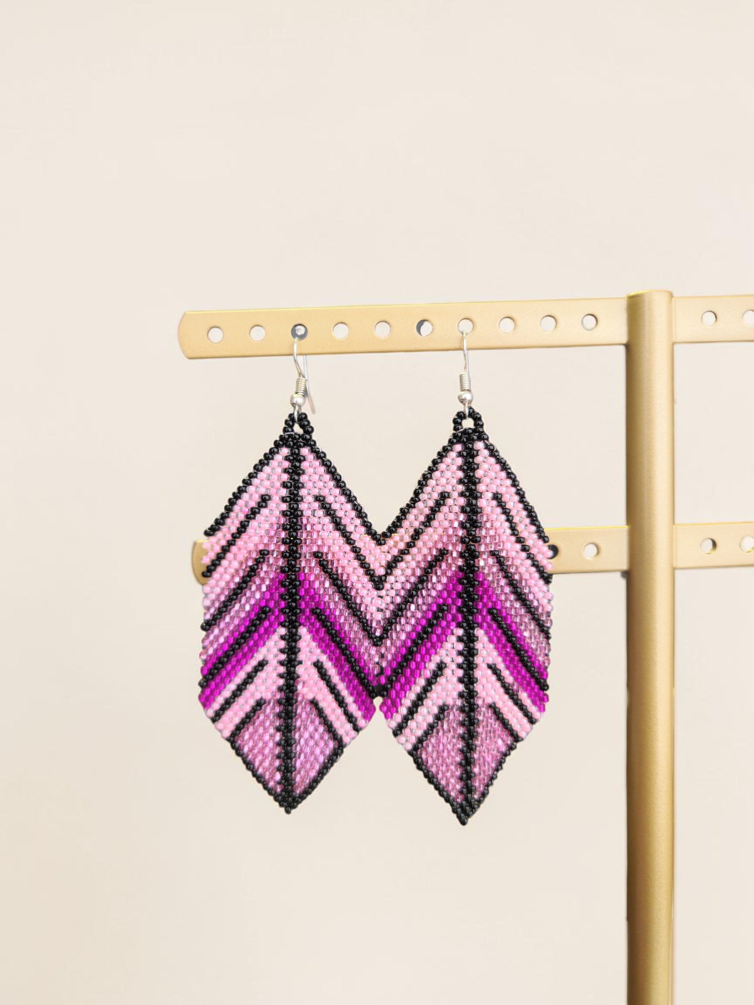 Pair of pink and black chevron pattern earrings on a gold earring stand against a beige background.