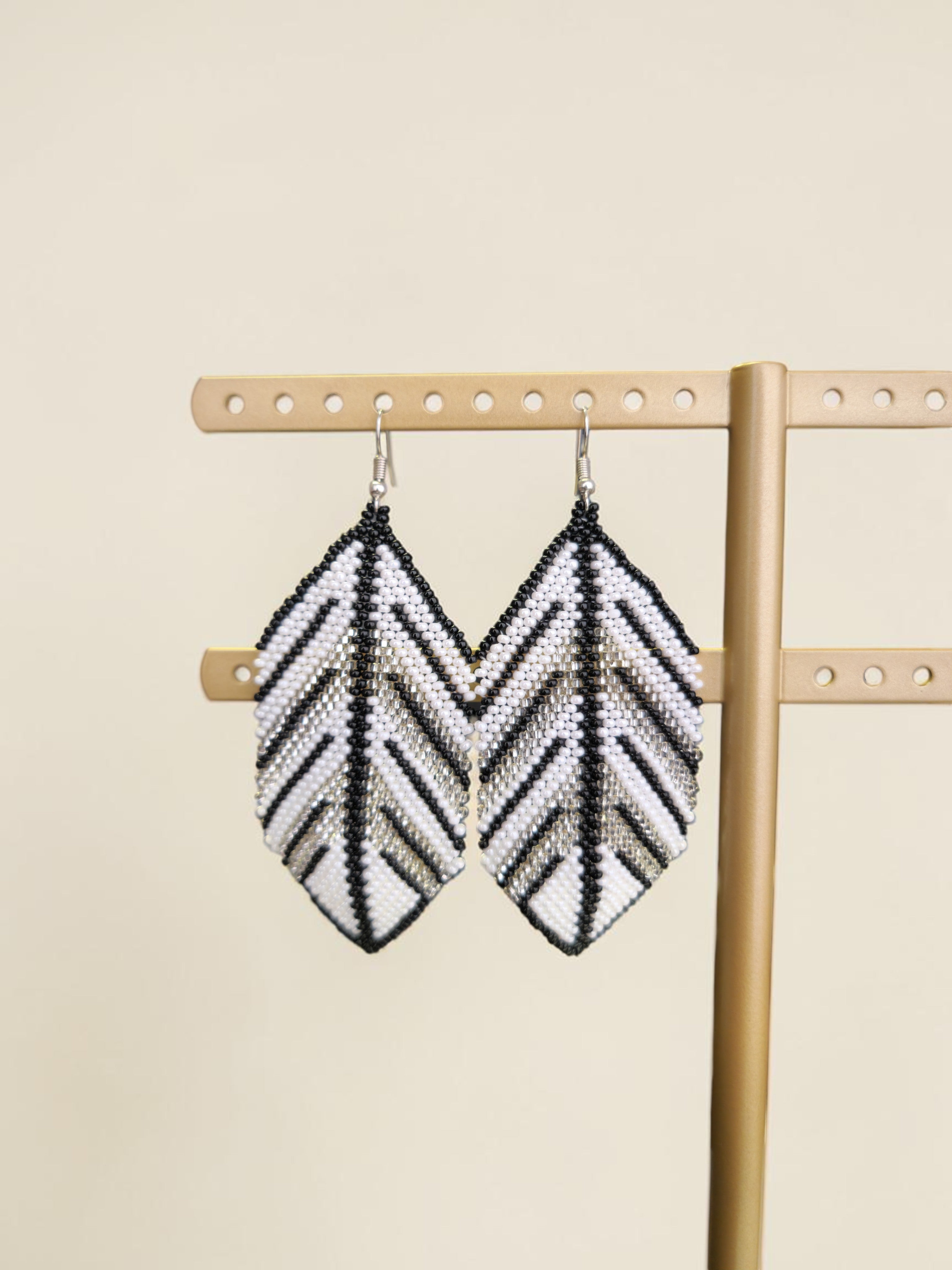 Black and white chevron patterned earrings hanging on a wooden rack against a beige background.