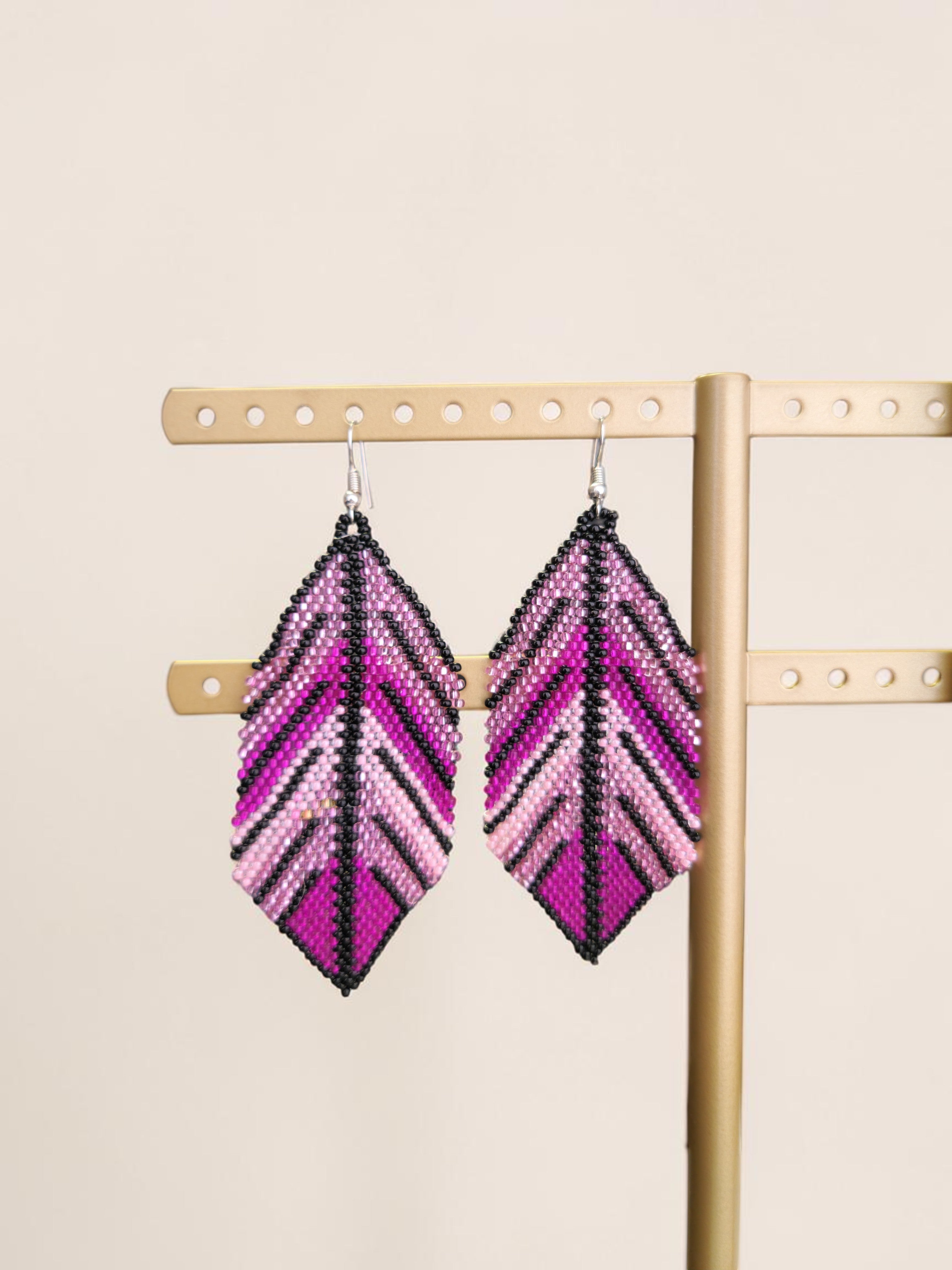 Pair of pink and purple chevron pattern earrings on a wooden stand.