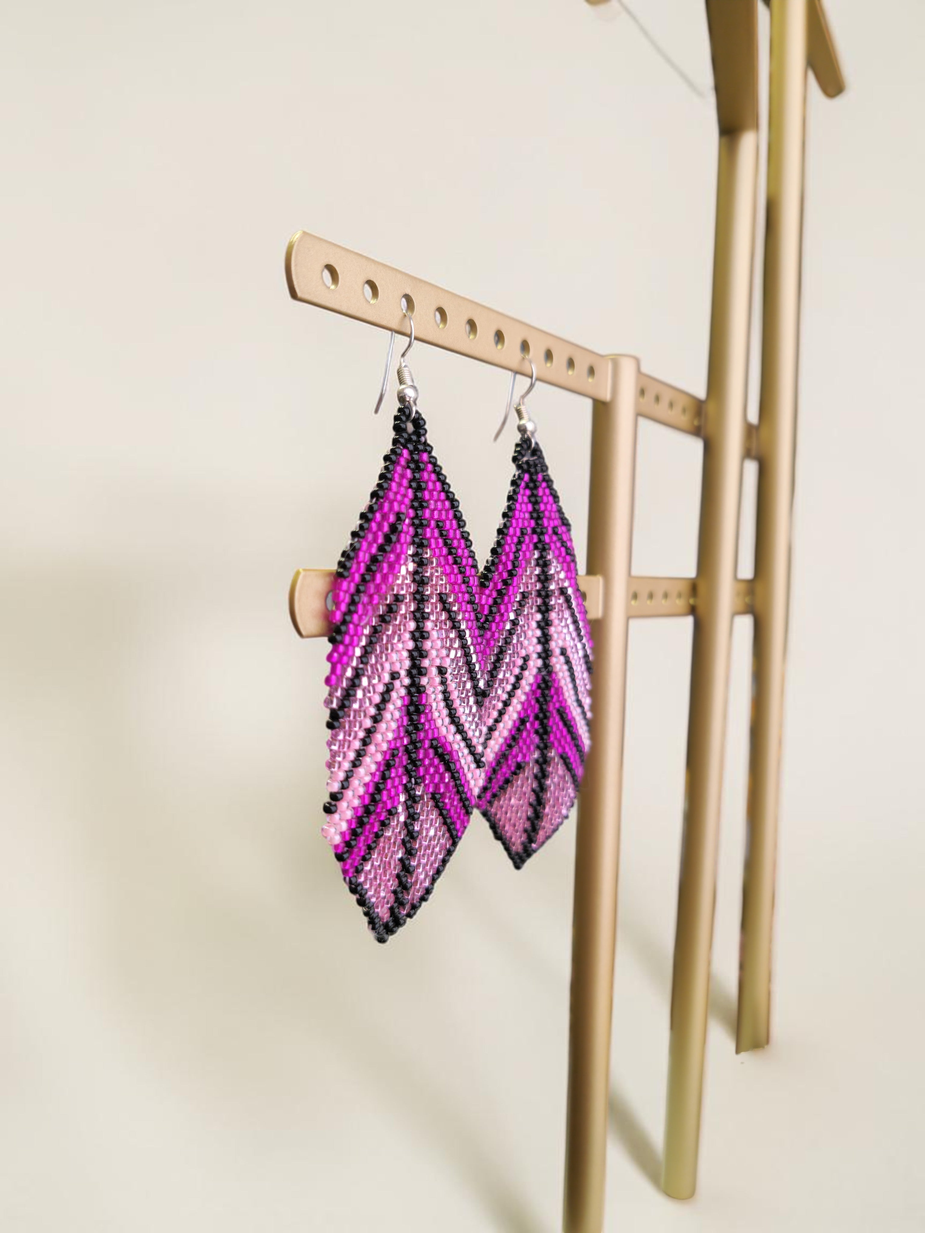 Purple and black beaded earrings on a gold stand against a beige background
