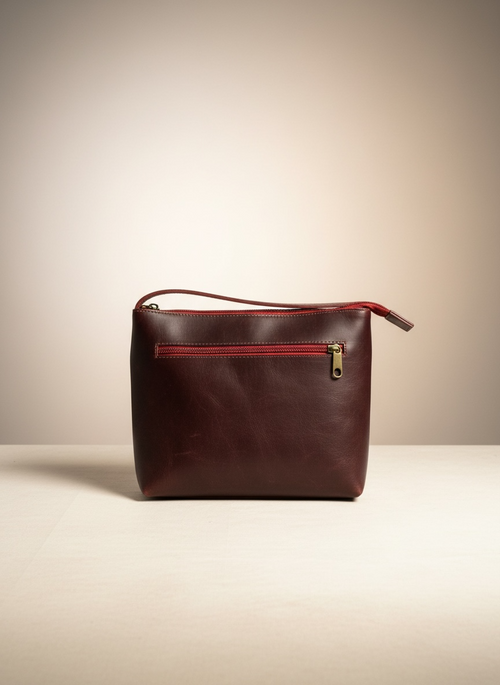 Brown leather handbag with a red zipper on a beige background